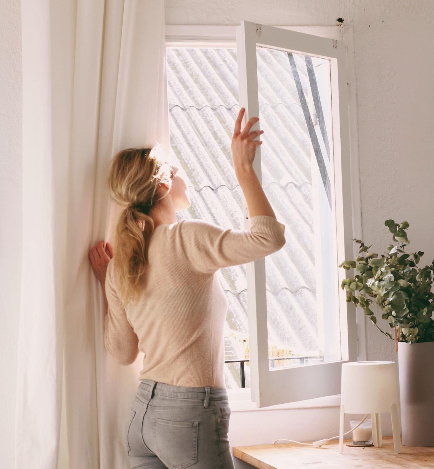 Woman opening window to increase ventilation and improve indoor air quality